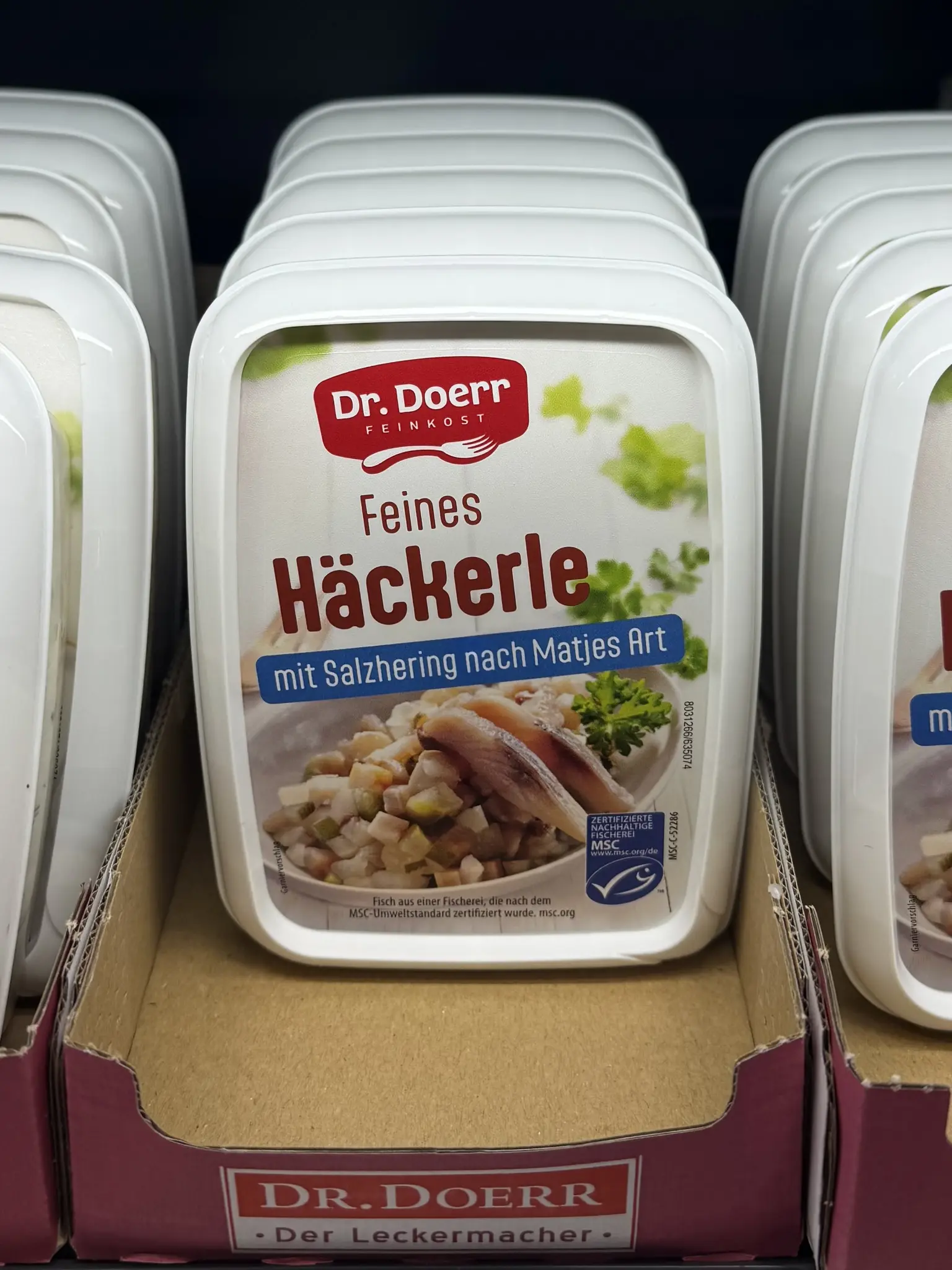 Product in a grocery store refrigerator: "Feines Häckerle, mit Salzhering nach Matjes Art", a fish salad. Translates to "good little hacker", but actually means "fine mince" or something like that