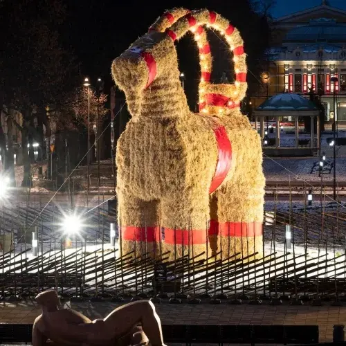 Photograph of the Gävle Goat at night. Giant straw goat statue with red ribbon decorations